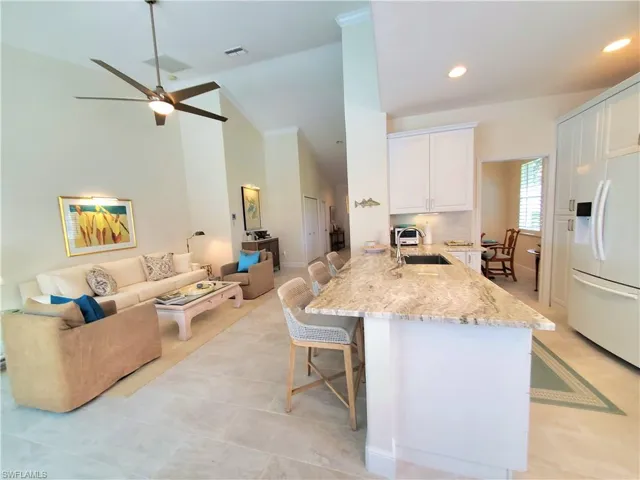 Kitchen featuring ceiling fan, white cabinetry, white refrigerator with ice dispenser, sink, and a breakfast bar