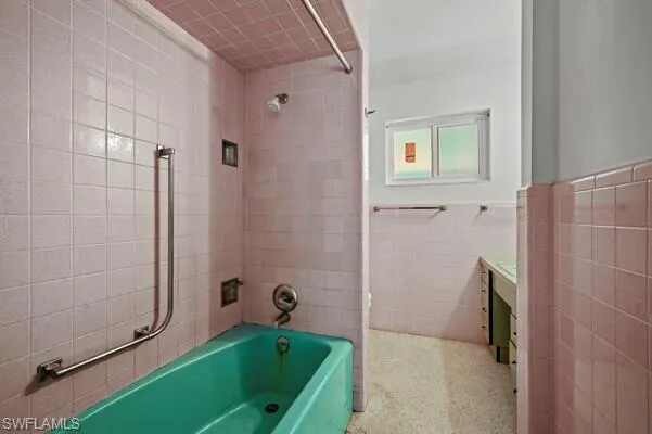 Bathroom with tile walls, tiled shower / bath, and vanity