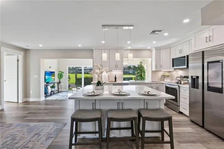 Kitchen featuring appliances with stainless steel finishes, white cabinetry, a kitchen island, pendant lighting, and a kitchen bar