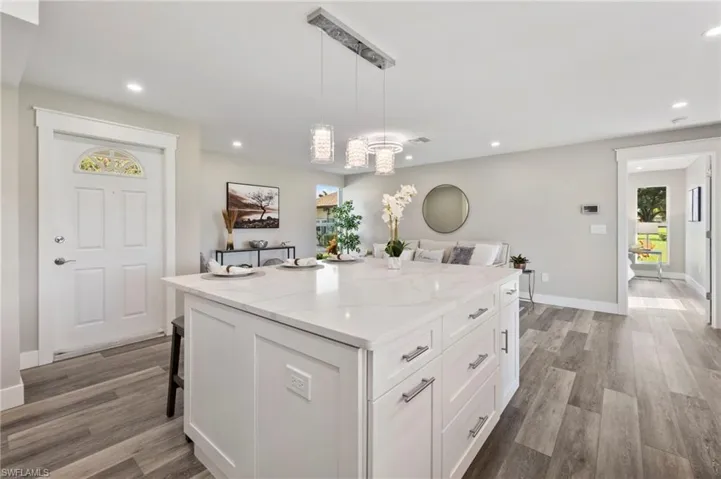 Kitchen with white cabinets, pendant lighting, a kitchen island, hardwood / wood-style flooring, and a breakfast bar