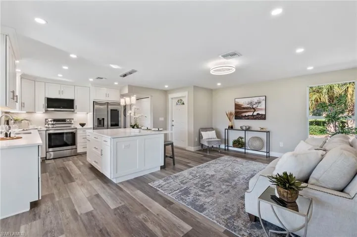 Kitchen featuring hanging light fixtures, white cabinets, a kitchen island, stainless steel appliances, and light wood-type flooring