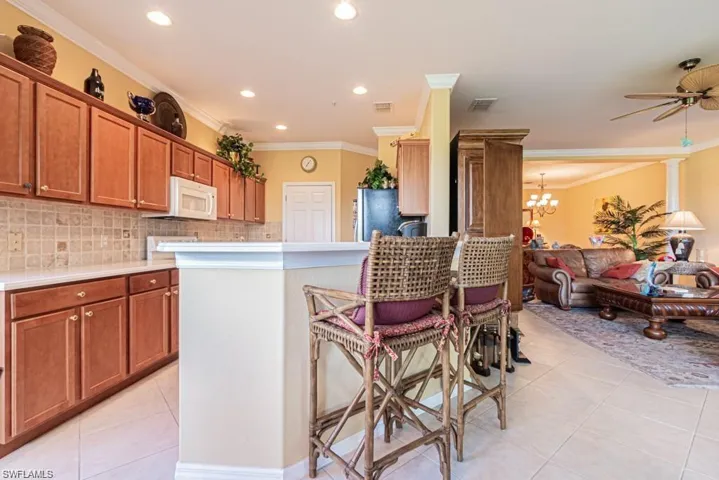Kitchen featuring ceiling fan with notable chandelier, crown molding, light tile patterned floors, tasteful backsplash, and stainless steel refrigerator