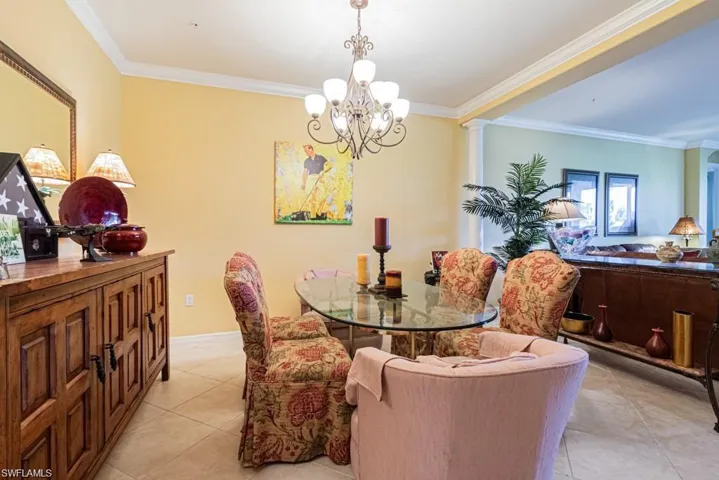 Dining space with light tile patterned floors, ornate columns, ornamental molding, and a notable chandelier