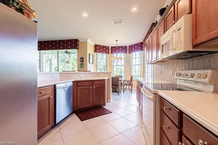Kitchen with decorative backsplash, stainless steel appliances, sink, light tile patterned floors, and decorative light fixtures