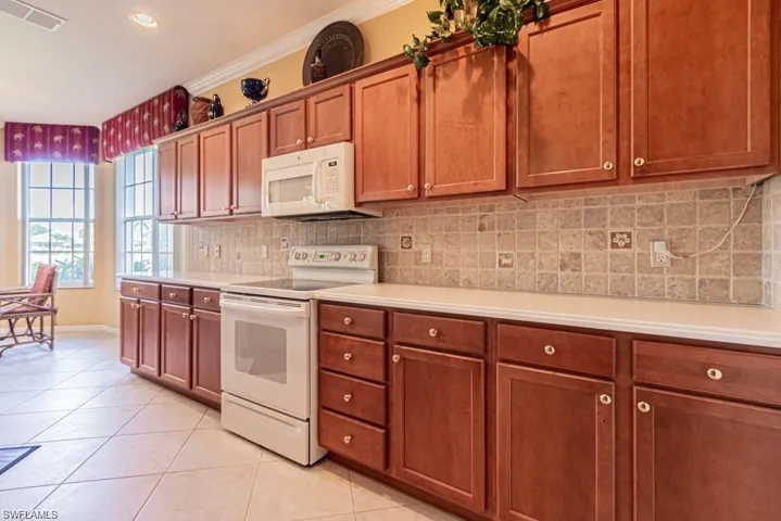 Kitchen with decorative backsplash, white appliances, ornamental molding, and light tile patterned floors