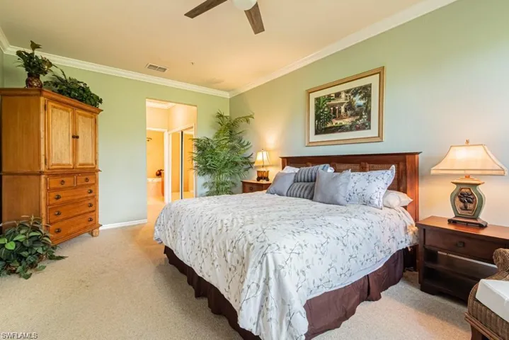 Carpeted bedroom with connected bathroom, ceiling fan, and ornamental molding