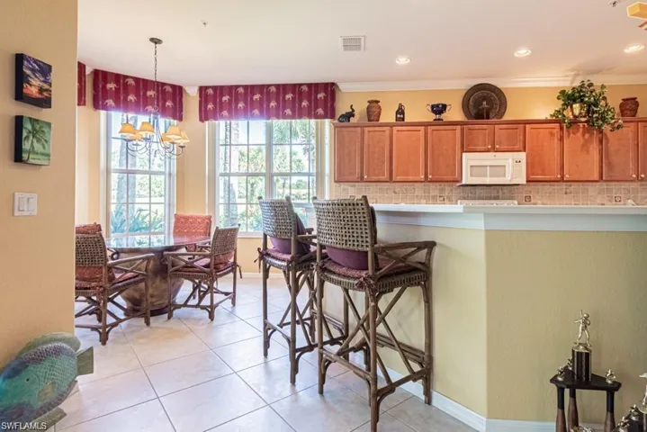 Kitchen featuring crown molding, decorative backsplash, decorative light fixtures, light tile patterned flooring, and a kitchen bar