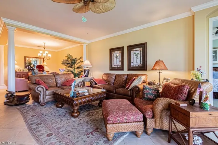Tiled living room with ornate columns, crown molding, and ceiling fan with notable chandelier
