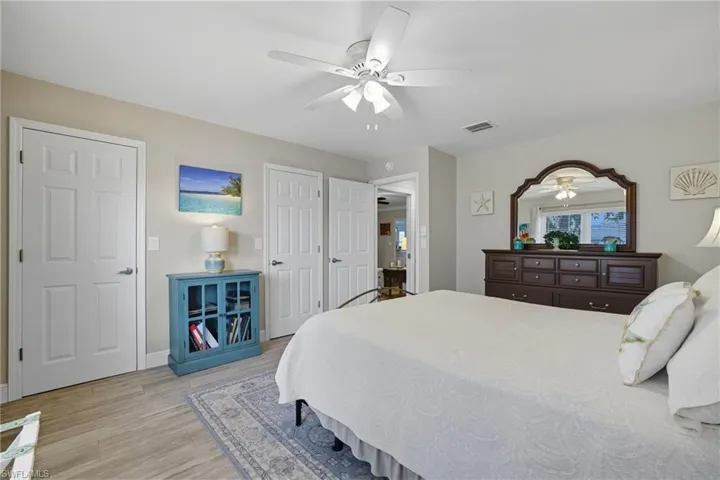 Bedroom featuring wood-finish flooring, a ceiling fan with integrated lighting, multiple paneled doors, and a decorative area rug