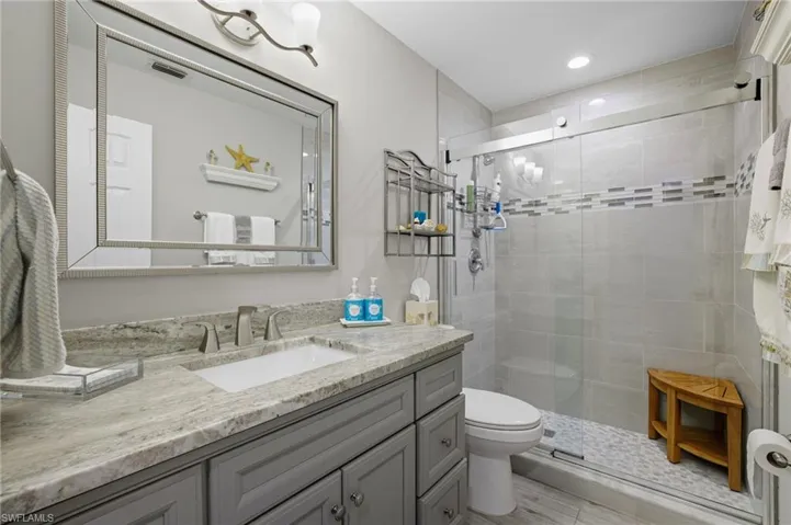 Bathroom featuring a gray vanity with an undermount sink, a light-toned patterned countertop, and a large framed mirror