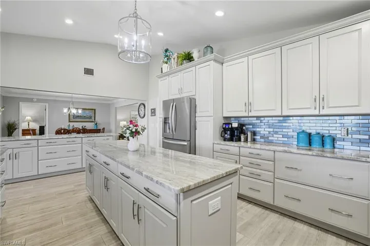 Spacious kitchen featuring an expansive center island with stone countertop, abundant white cabinetry, stainless steel appliances, and wood-finish flooring