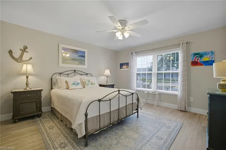 Spacious room featuring wood-finish flooring, a ceiling fan, and a large window with horizontal blinds and decorative curtains