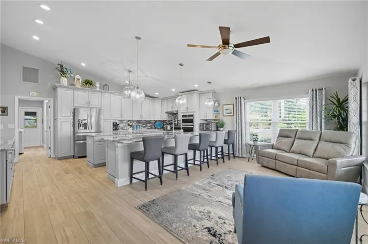 Open-concept kitchen and living area featuring high vaulted ceilings, light wood-finish flooring, a kitchen island with seating, a built-in oven, and pendant lighting