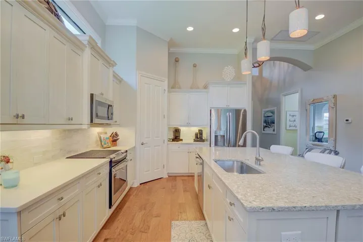 Kitchen featuring appliances with stainless steel finishes, crown molding, an island with sink, light wood-style floors, and hanging light fixtures
