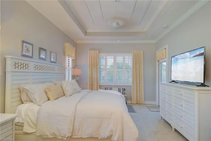 Bedroom with a raised ceiling, light carpet, and crown molding