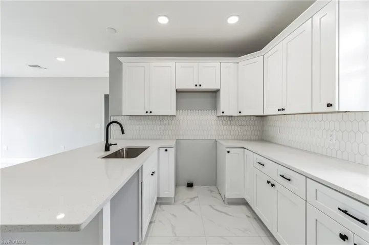 Kitchen featuring light stone countertops, tasteful backsplash, light tile flooring, sink, and white cabinetry
