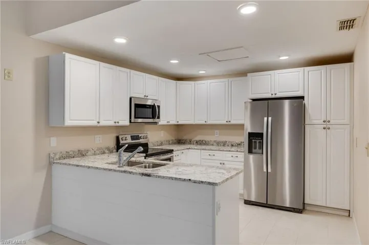 Kitchen with stainless steel appliances, white cabinets, light stone counters, a peninsula, and recessed lighting