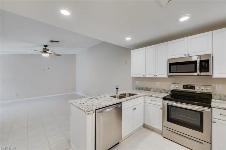 Kitchen with stainless steel appliances, white cabinets, light stone counters, a peninsula, and a ceiling fan
