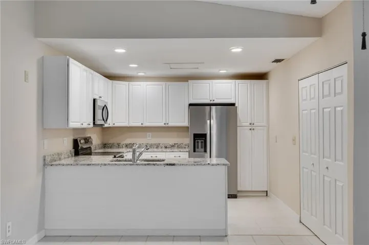 Kitchen featuring light stone countertops, white cabinetry, appliances with stainless steel finishes, recessed lighting, and a peninsula