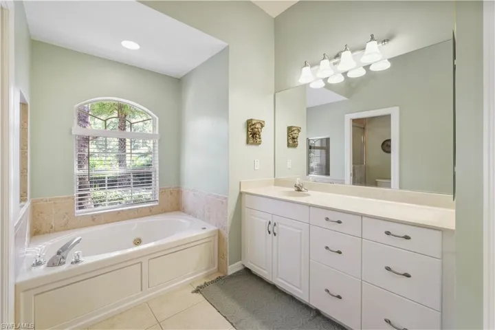 Bathroom with a jetted tub, light tile patterned floors, vanity, and an enclosed shower
