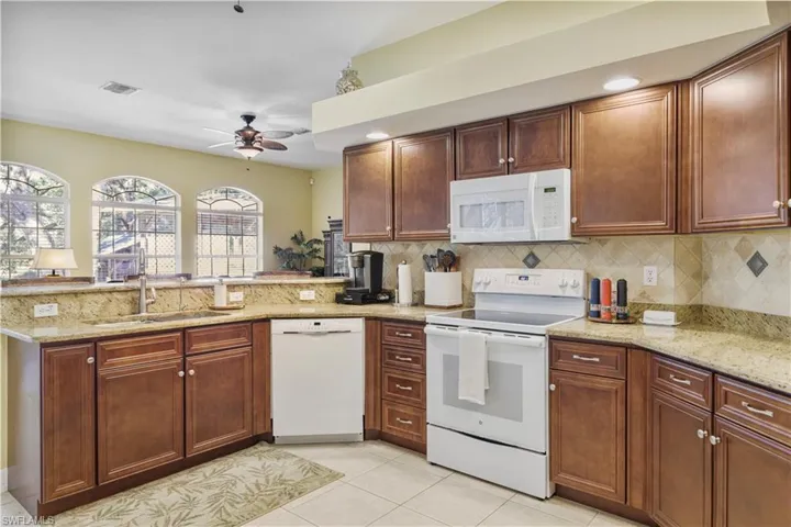 Kitchen featuring white appliances, a peninsula, light stone counters, and light tile patterned flooring