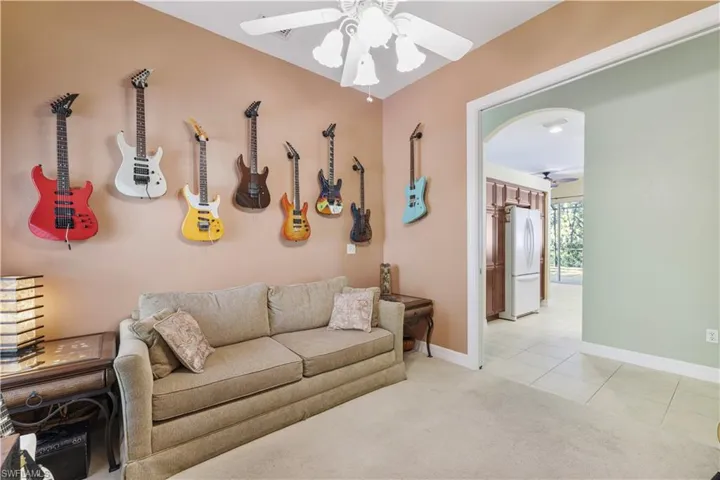 Living area with a ceiling fan, light carpet, light tile patterned floors, and arched walkways