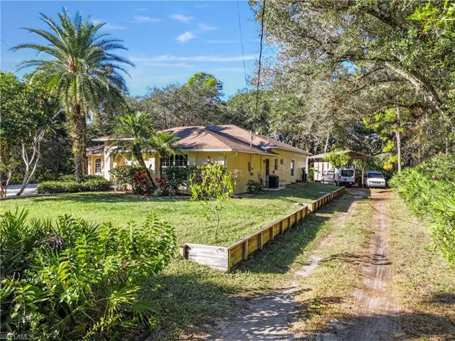 View of front of property featuring a front yard, stucco siding, driveway, and view of wooded area