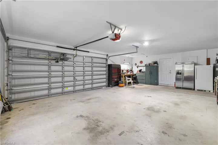Garage featuring stainless steel refrigerator with ice dispenser, freestanding refrigerator, and a garage door opener