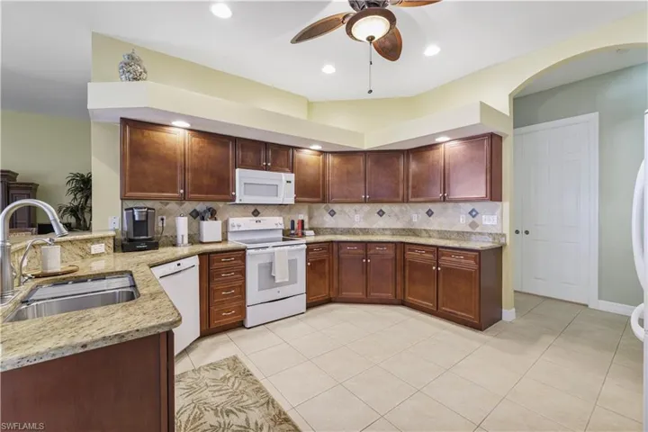 Kitchen featuring white appliances, light stone counters, a peninsula, and ceiling fan