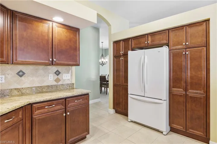 Kitchen with freestanding refrigerator, light stone counters, arched walkways, light tile patterned flooring, and backsplash