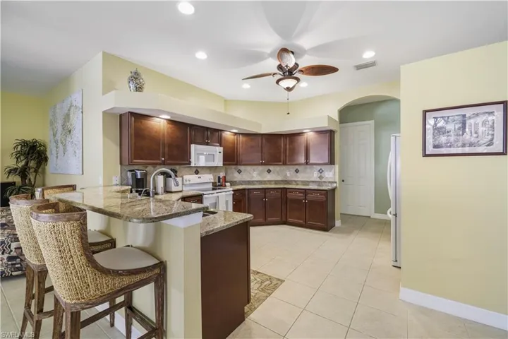 Kitchen featuring a peninsula, a kitchen breakfast bar, light stone counters, white appliances, and light tile patterned floors