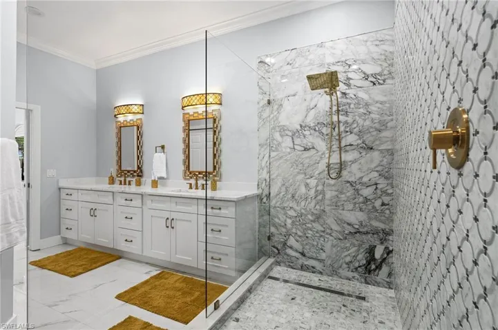 Bathroom with crown molding, a marble finish shower, light marble finish flooring, and double vanity