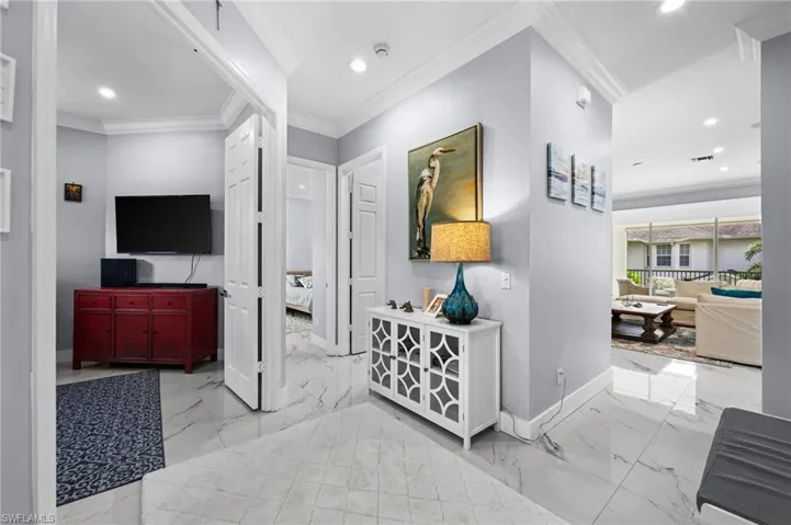 Hall with ornamental molding, light marble finish floors, and recessed lighting