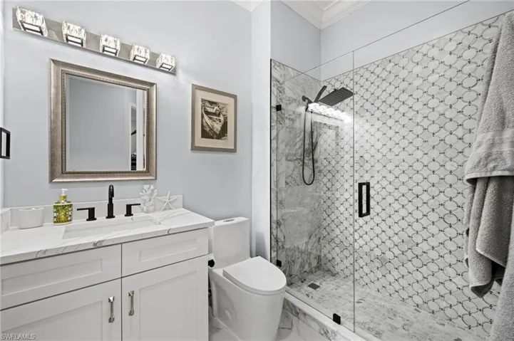 Full bath featuring vanity, a shower stall, ornamental molding, and marble finish flooring