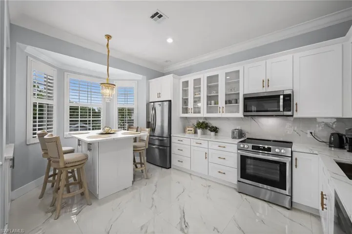 Kitchen featuring stainless steel appliances, white cabinets, light marble finish flooring, crown molding, and decorative backsplash
