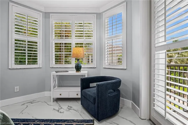 Living area with healthy amount of natural light, light marble finish floors, and crown molding