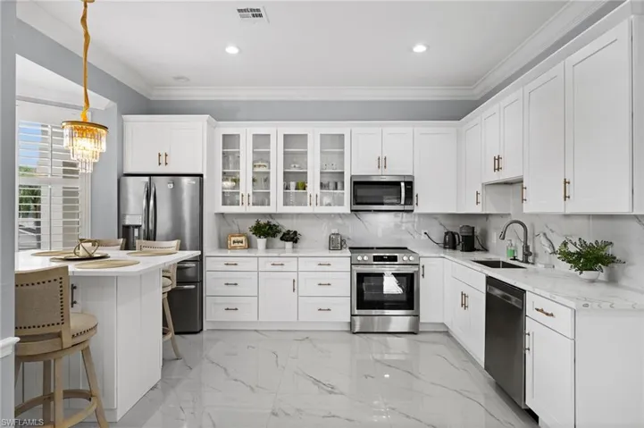 Kitchen featuring ornamental molding, light marble finish flooring, appliances with stainless steel finishes, backsplash, and white cabinetry