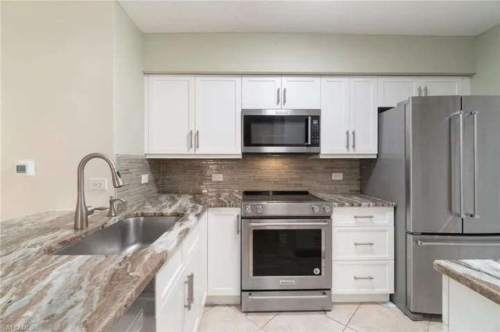 Kitchen featuring light tile patterned floors, light stone counters, stainless steel appliances, a sink, and decorative backsplash