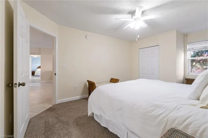 Carpeted bedroom with a textured ceiling, ceiling fan, baseboards, a closet, and tile patterned floors
