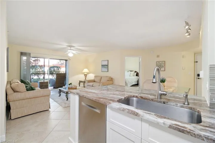 Kitchen featuring stainless steel dishwasher, open floor plan, white cabinetry, a sink, and light stone countertops