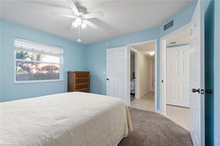 Carpeted bedroom with tile patterned flooring, visible vents, ceiling fan, and a textured ceiling