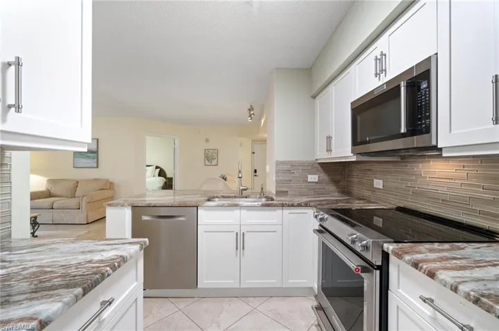 Kitchen with light stone counters, stainless steel appliances, tasteful backsplash, a sink, and a peninsula