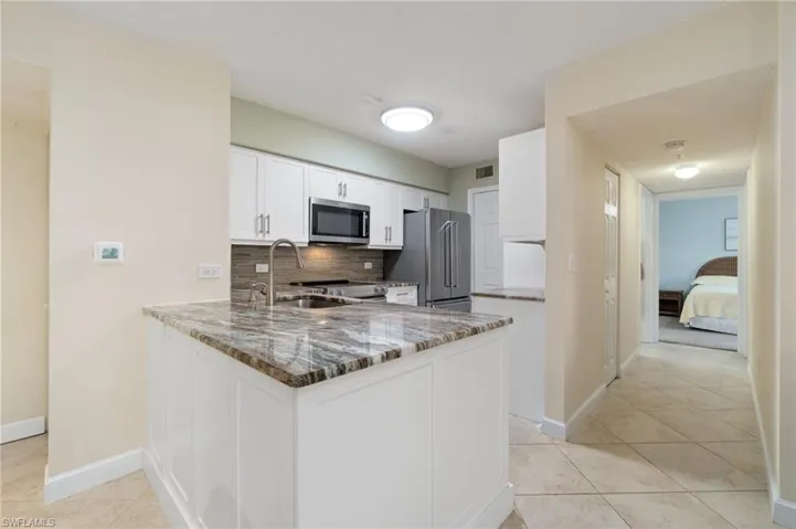 Kitchen featuring decorative backsplash, stainless steel appliances, stone counters, white cabinetry, and a sink