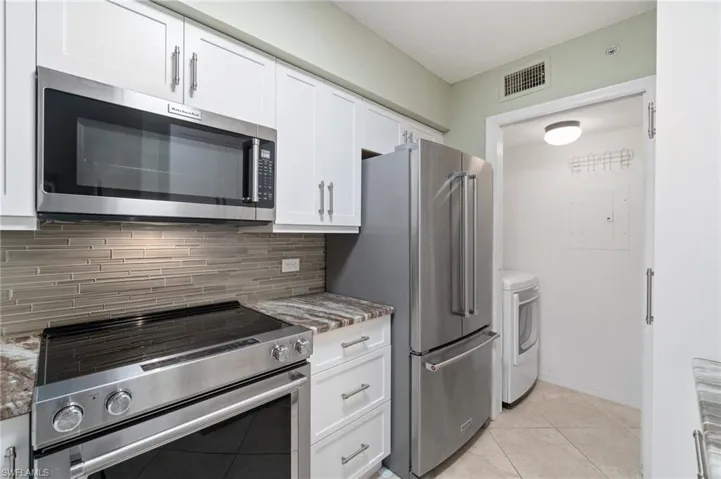 Kitchen featuring visible vents, white cabinetry, appliances with stainless steel finishes, tasteful backsplash, and washer and clothes dryer