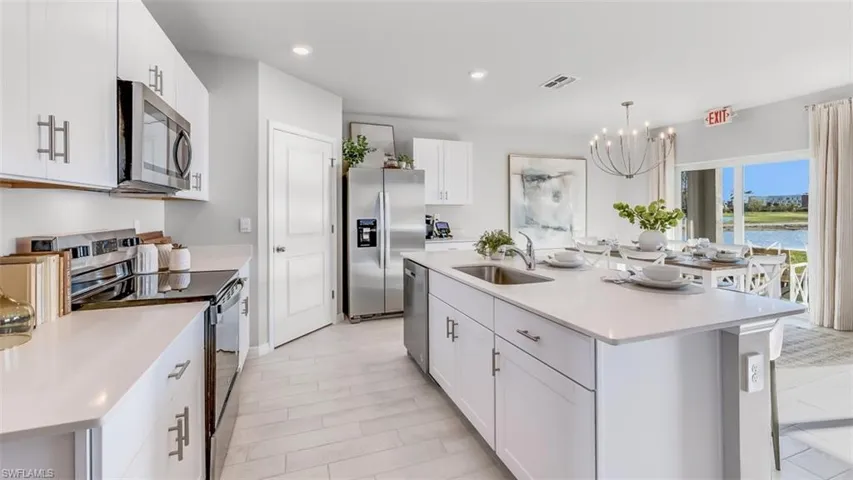 Model home. Kitchen featuring an island with sink, stainless steel appliances, white cabinets, a chandelier, and light stone counters