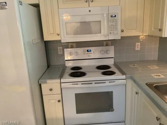 Kitchen with white appliances, tile counters, white cabinets, and backsplash