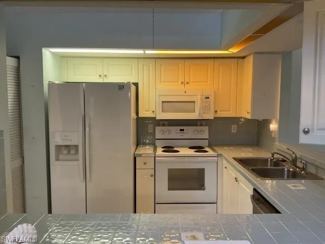 Kitchen with tile counters, white appliances, tasteful backsplash, and white cabinetry