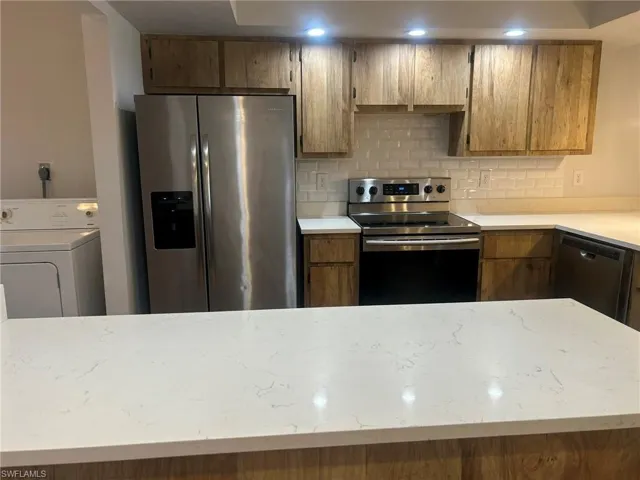 Kitchen with light stone counters, tasteful backsplash, brown cabinets, washer / clothes dryer, and stainless steel appliances