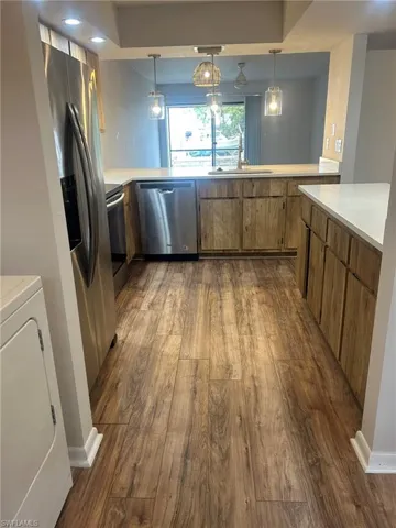 Kitchen with light countertops, stainless steel dishwasher, a sink, dark wood-style floors, and washer / dryer