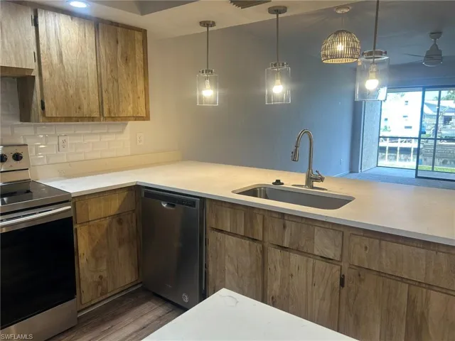 Kitchen featuring light countertops, a sink, pendant lighting, stainless steel appliances, and dark wood-type flooring
